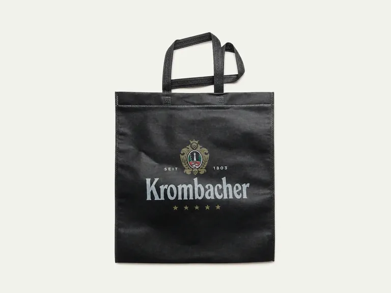 Кромбахер — чёрная многоразовая сумка из спанбонда с длинными ручками и серебристой печатью логотипа.